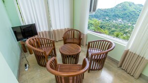 Un balcón con mobiliario de madera, televisor y vistas a una ladera verde.