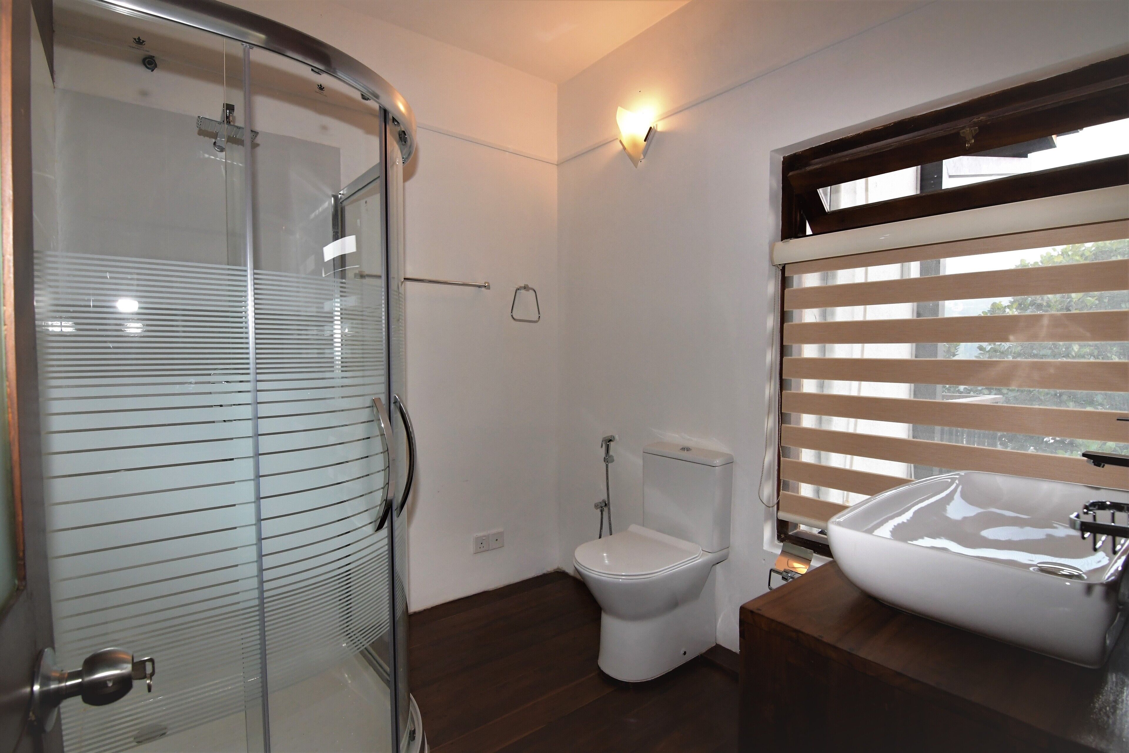 A modern bathroom with a glass shower enclosure, a toilet, and a large sink with a window above it.