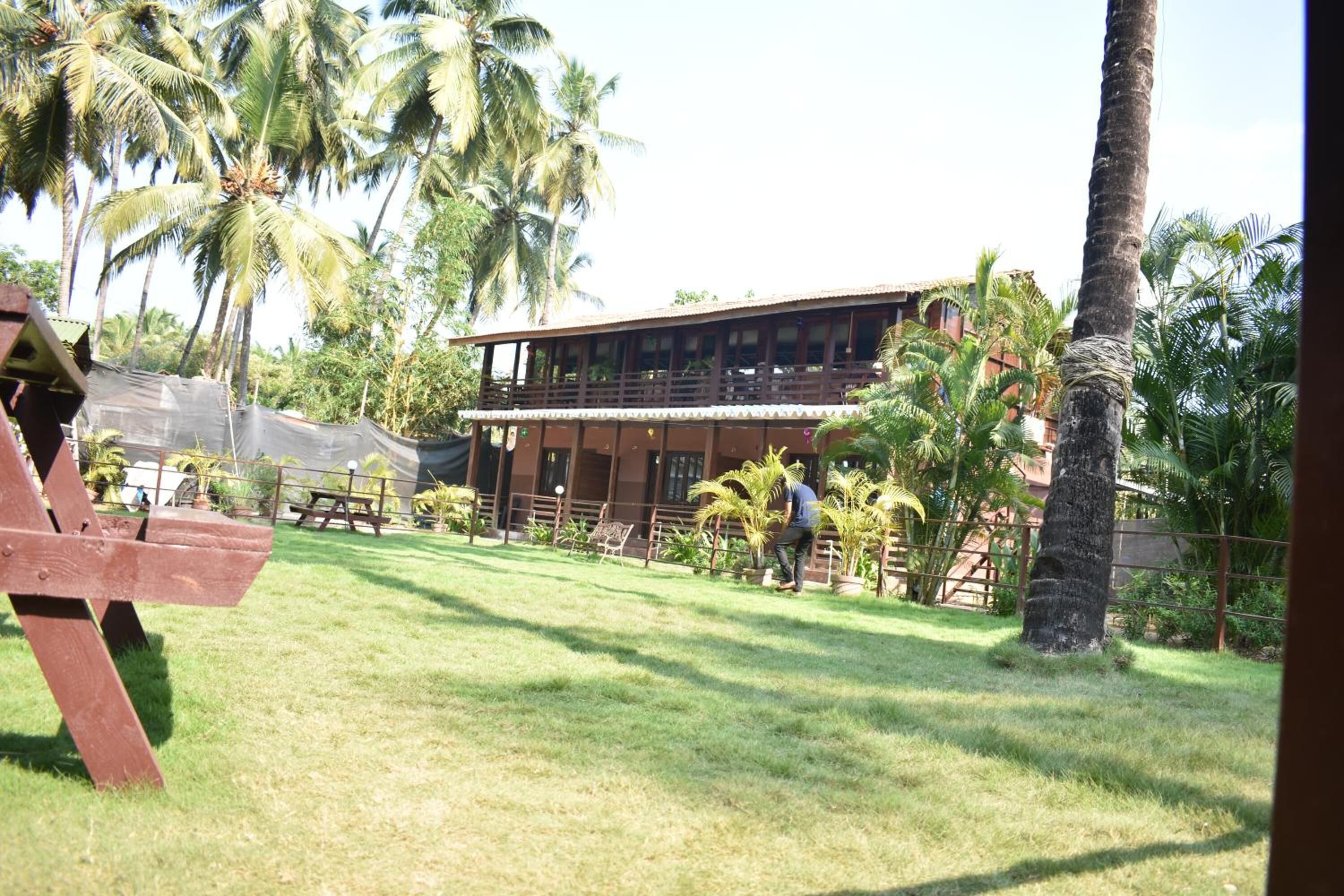 A two-story building with a flat roof, surrounded by palm trees and a grassy area.