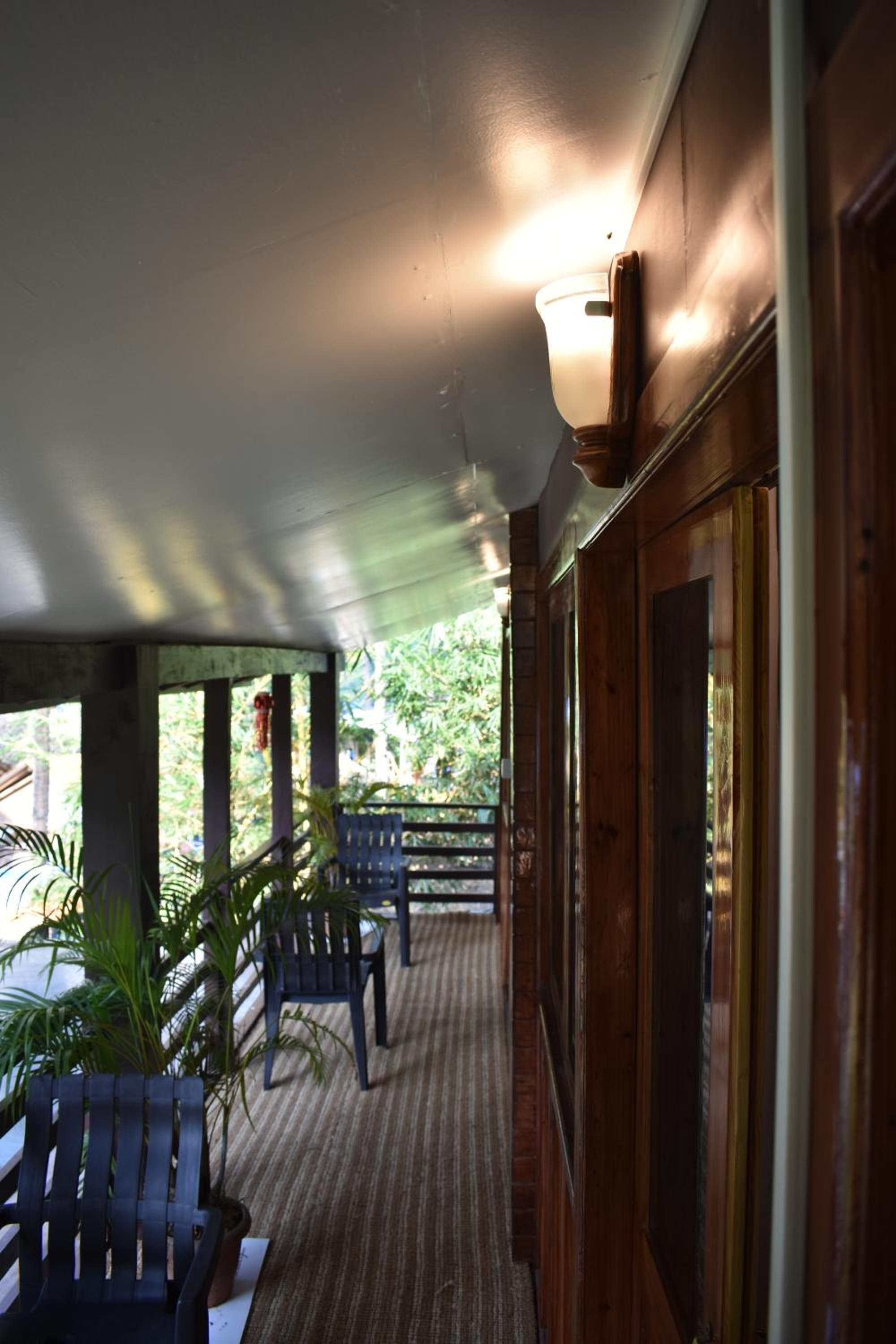 Une véranda couverte avec des balustrades en bois, des chaises et des plantes en pot.