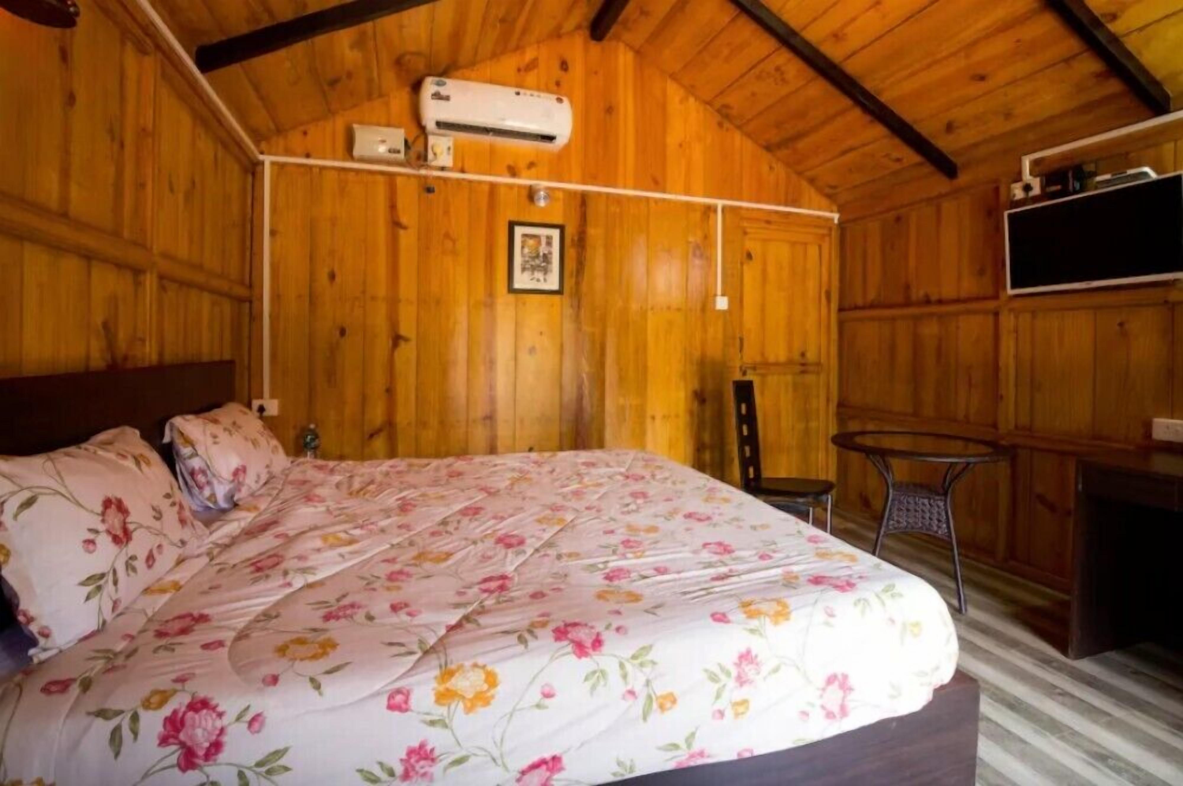 A wooden room with a bed, a small table, and an air conditioning unit.