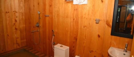 A wooden-paneled bathroom with a toilet, sink, and shower.
