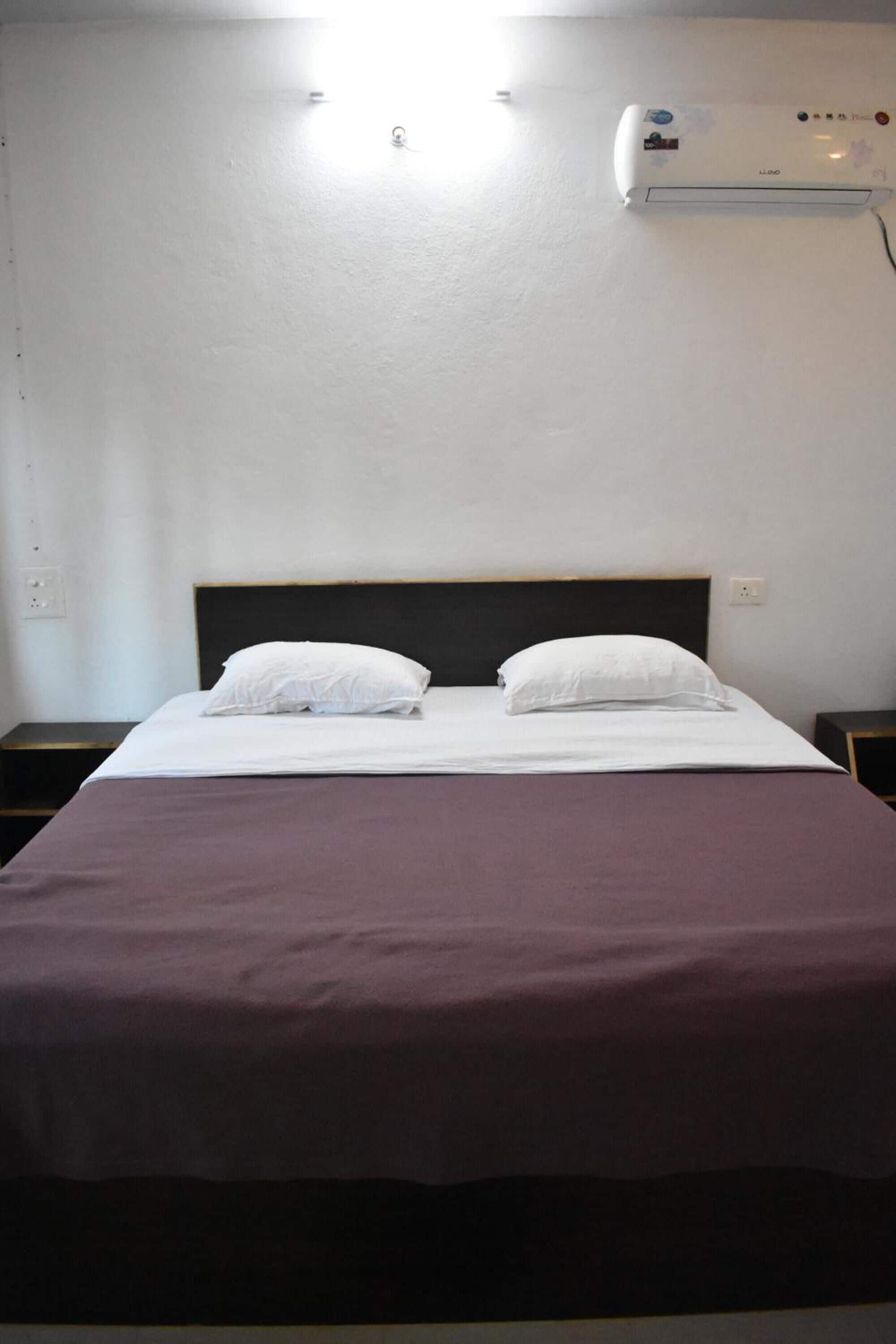 A single bed with a headboard, a bedside table, and a wall-mounted air conditioning unit.