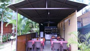 Un patio al aire libre con mesas y sillas, una zona de estar cubierta y una cocina al fondo.