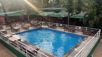 Una piscina con sillas de descanso y sombrillas, rodeada de follaje.