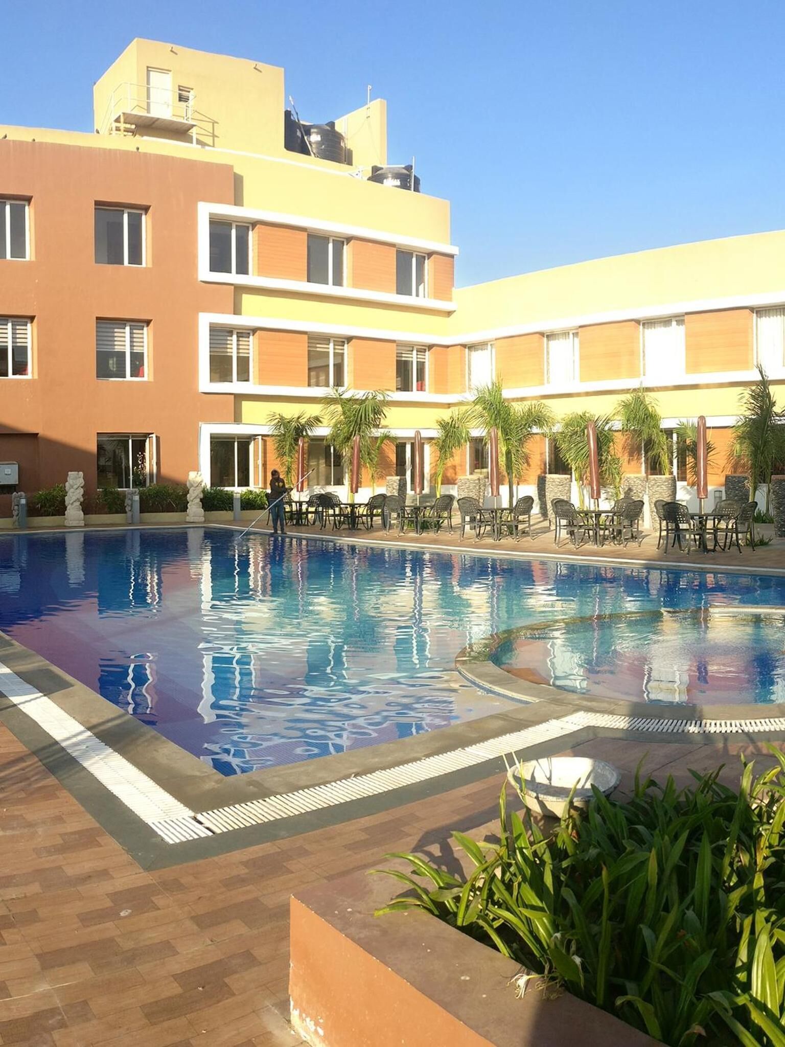 En swimmingpool med liggestole og palmer, omgivet af en bygning med flere balkoner.