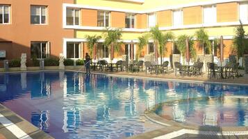 En swimmingpool med liggestole og palmer, omgivet af en bygning med flere balkoner.