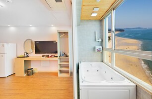 A modern bathroom with a bathtub, a large mirror, and a view of the beach.