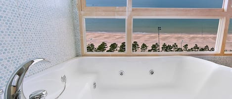 A bathroom with a large bathtub, a shower, and a view of the beach through a window.
