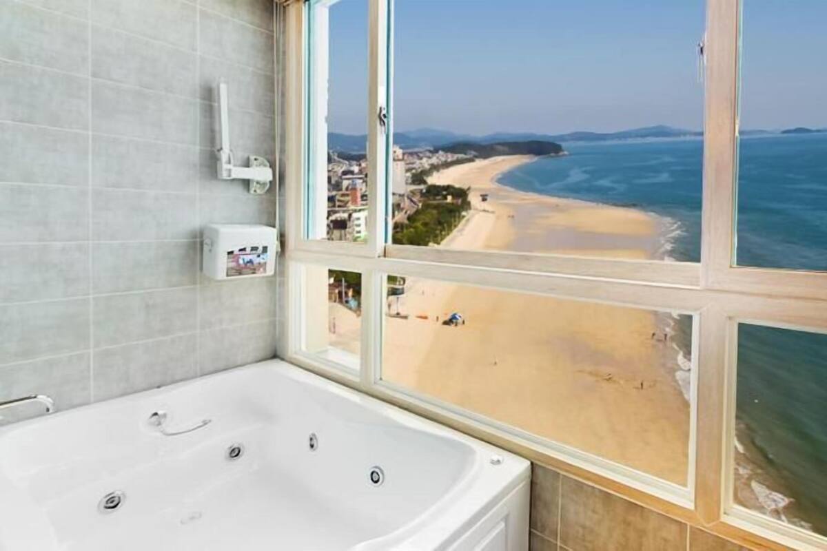 Un baño con bañera, una ventana de múltiples paneles y vista a la playa y al océano.