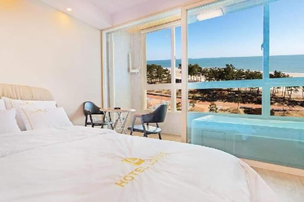 Habitación de hotel con cama, una mesita, dos sillas y un ventanal con vistas a la playa.
