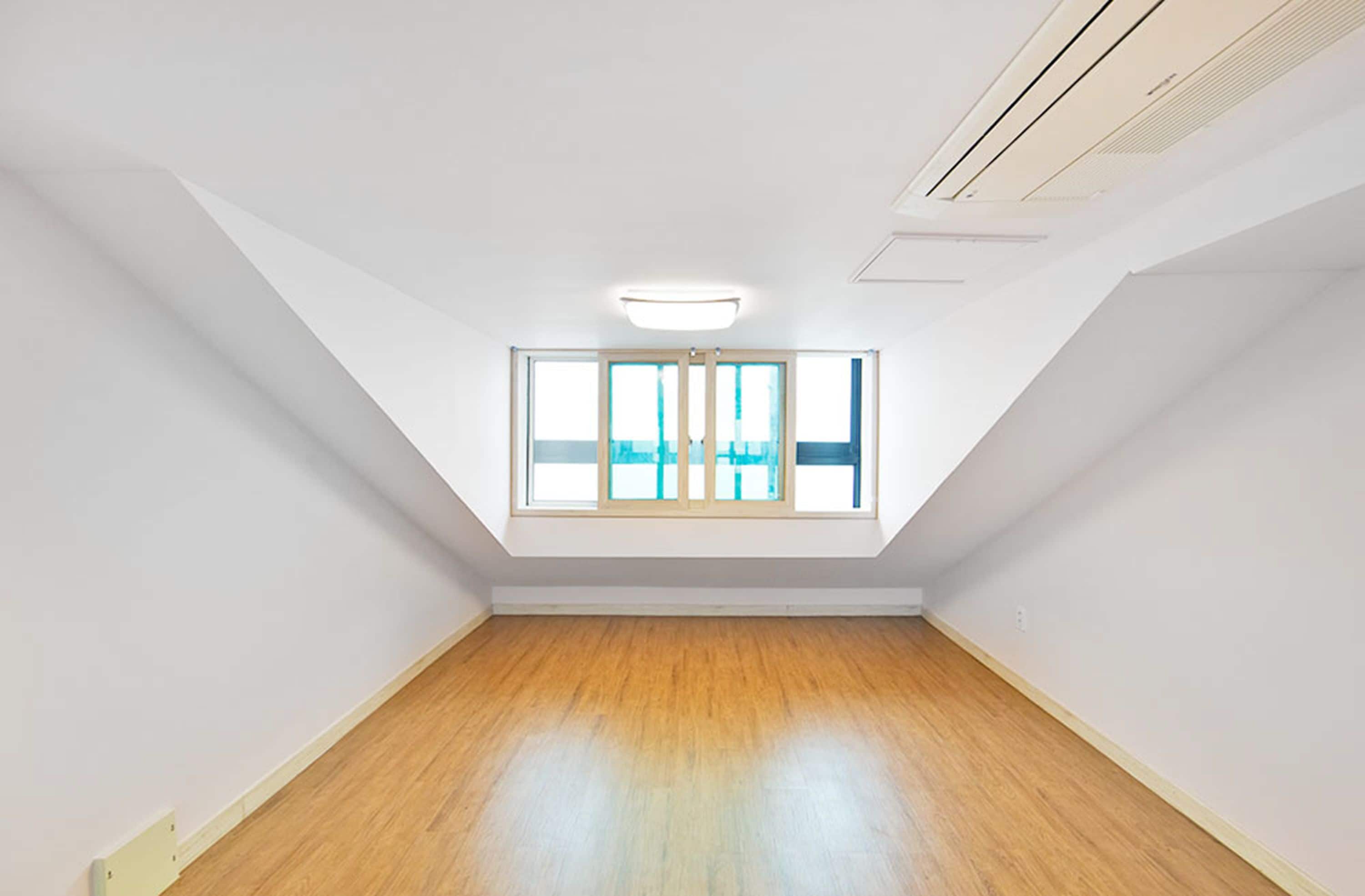 A room with a sloped ceiling, a skylight, and wooden flooring.