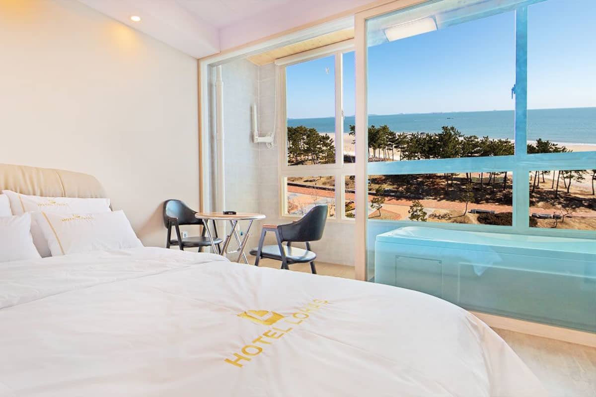 Habitación de hotel con cama, una mesita, dos sillas y un ventanal con vistas a la playa.