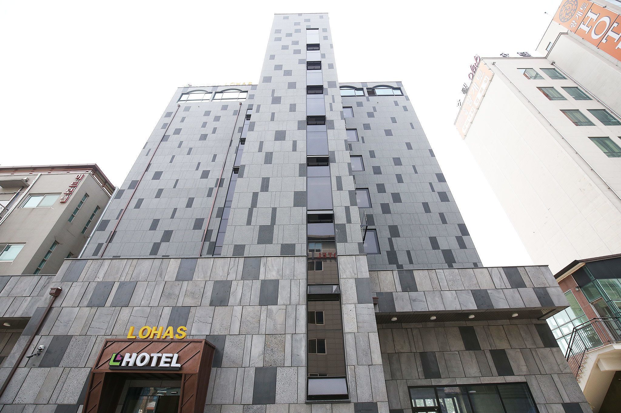 A tall hotel building with a modern design, featuring a prominent entrance and a sign for "LOHAS HOTEL".