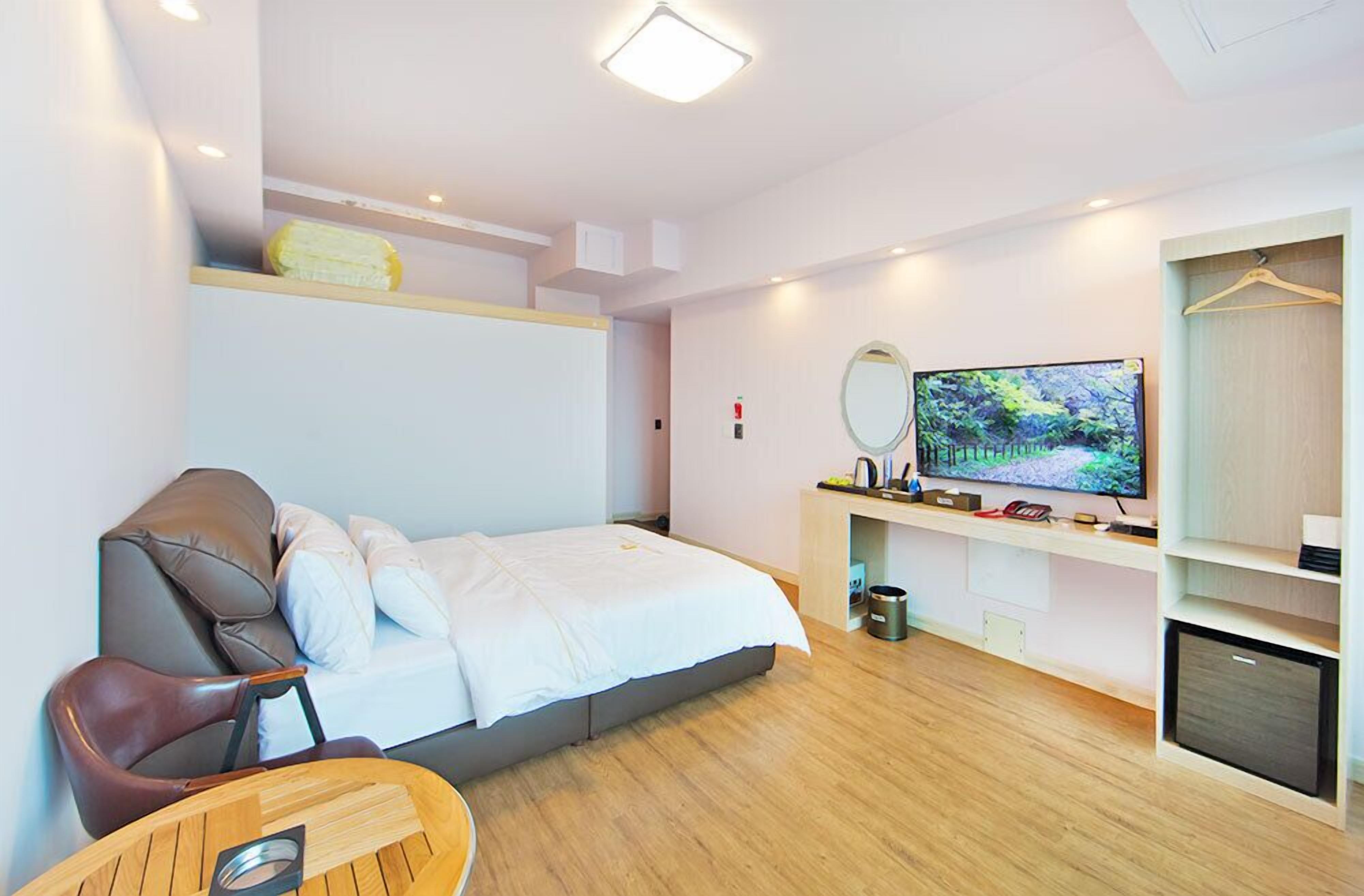 A modern hotel room with a bed, a TV, a seating area, and a wardrobe.