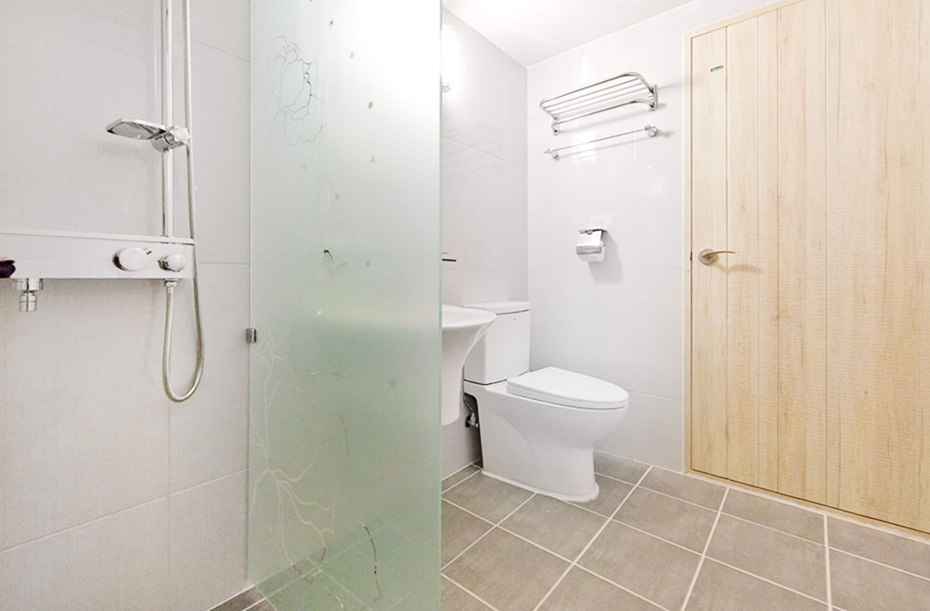 Et badeværelse med brusekabine i glas, toilet og trædør.