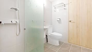 Et badeværelse med brusekabine i glas, toilet og trædør.