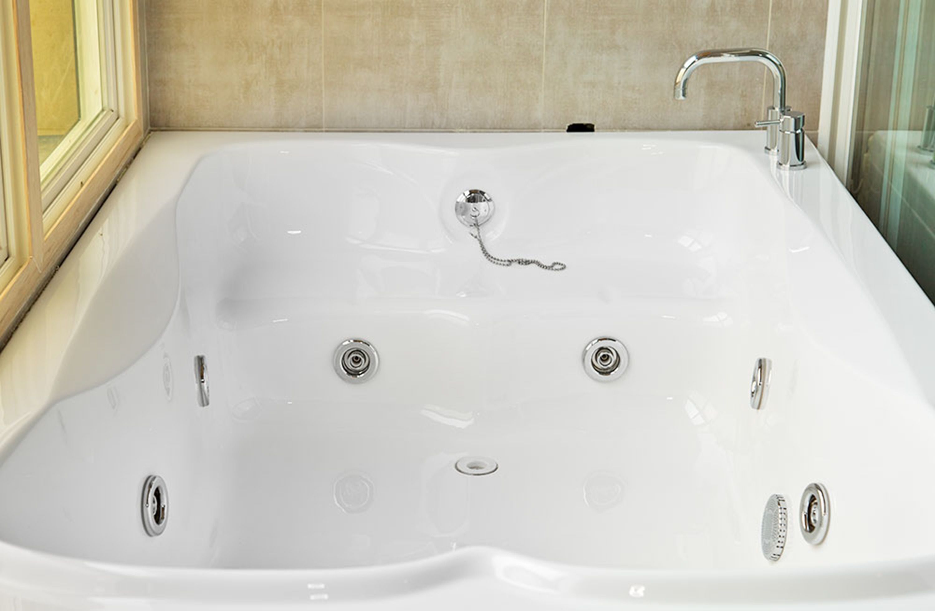 A large, rectangular, white bathtub with multiple faucets and a drain.