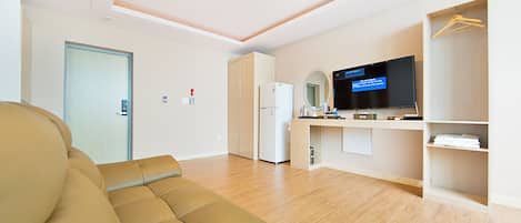 A modern living room with a beige sofa, a flat-screen TV, a refrigerator, and a wooden floor.