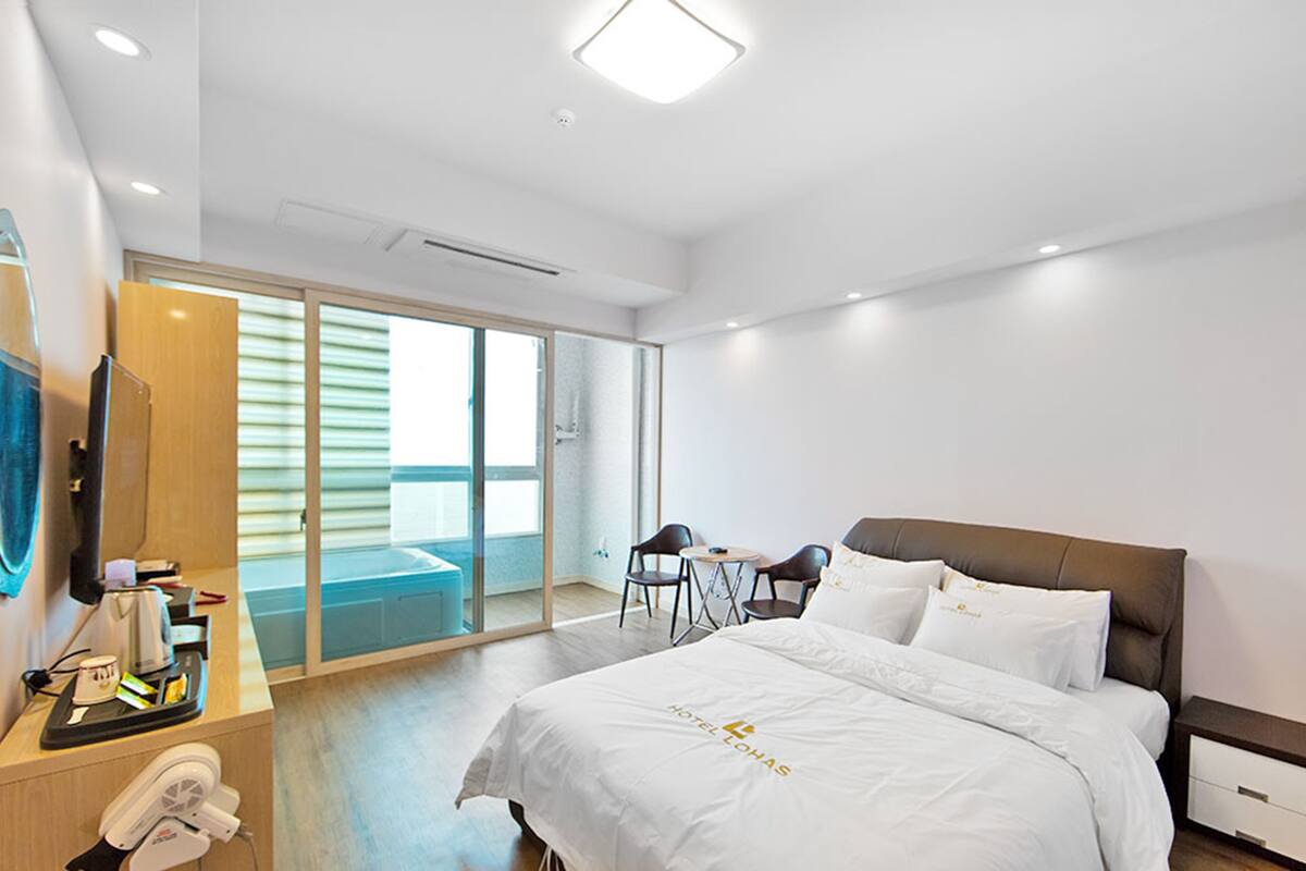 Habitación de hotel con cama, escritorio con teléfono, cafetera y vista al exterior.