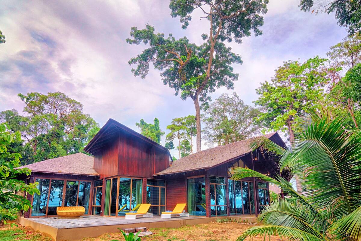 A modern house with large glass windows, a wooden exterior, and a patio with lounge chairs.