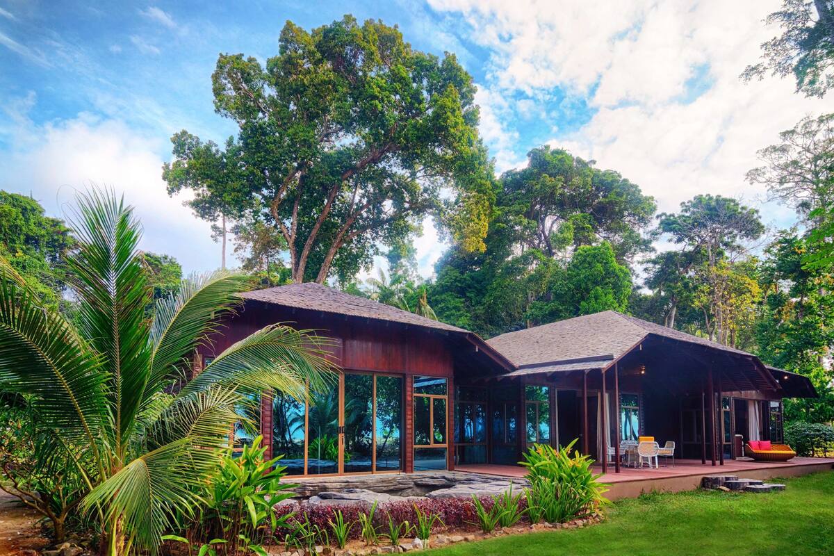 A modern building with large glass windows, surrounded by lush greenery and trees.