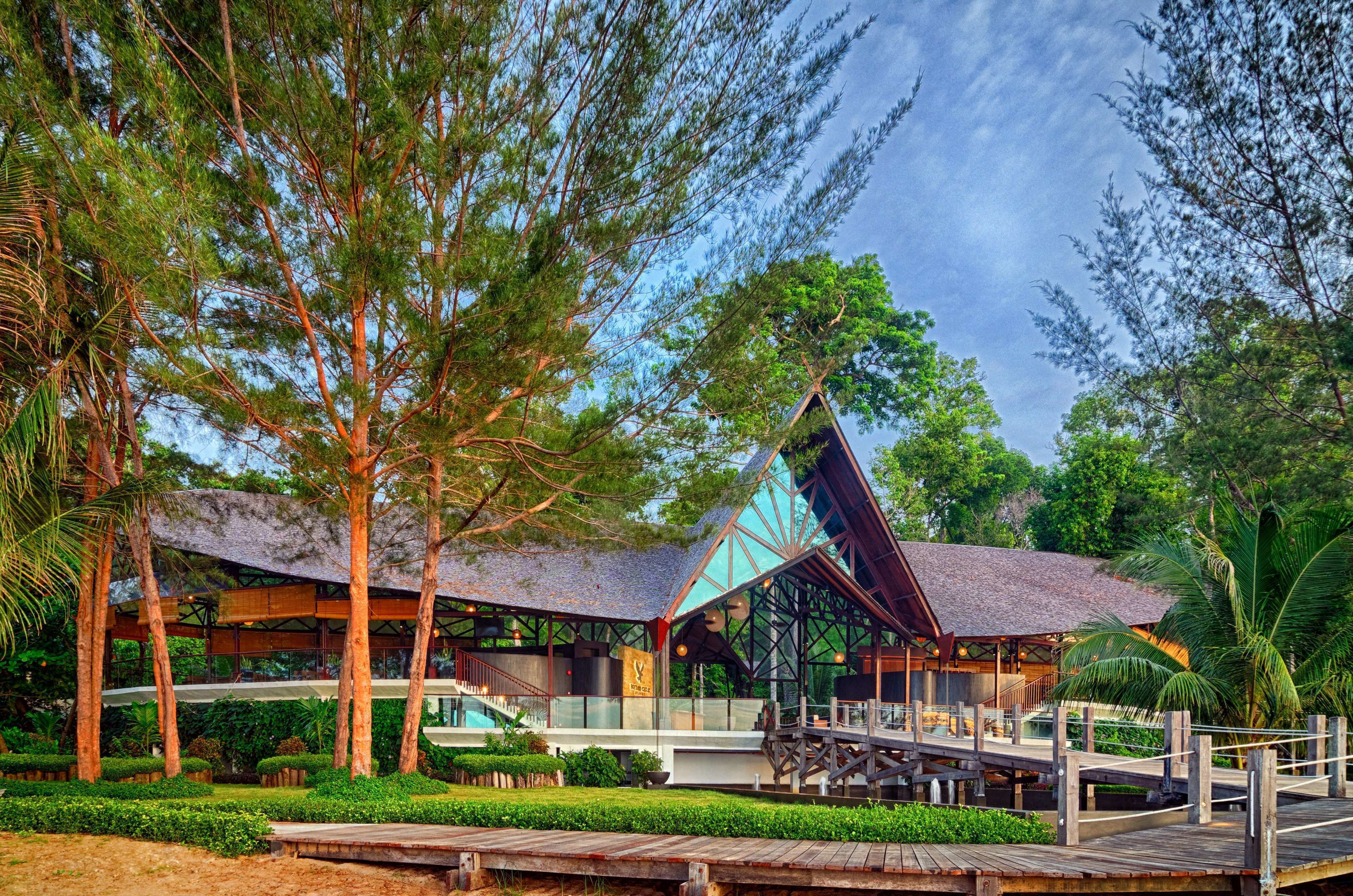 A modern building with a glass facade, surrounded by lush greenery and a wooden deck.