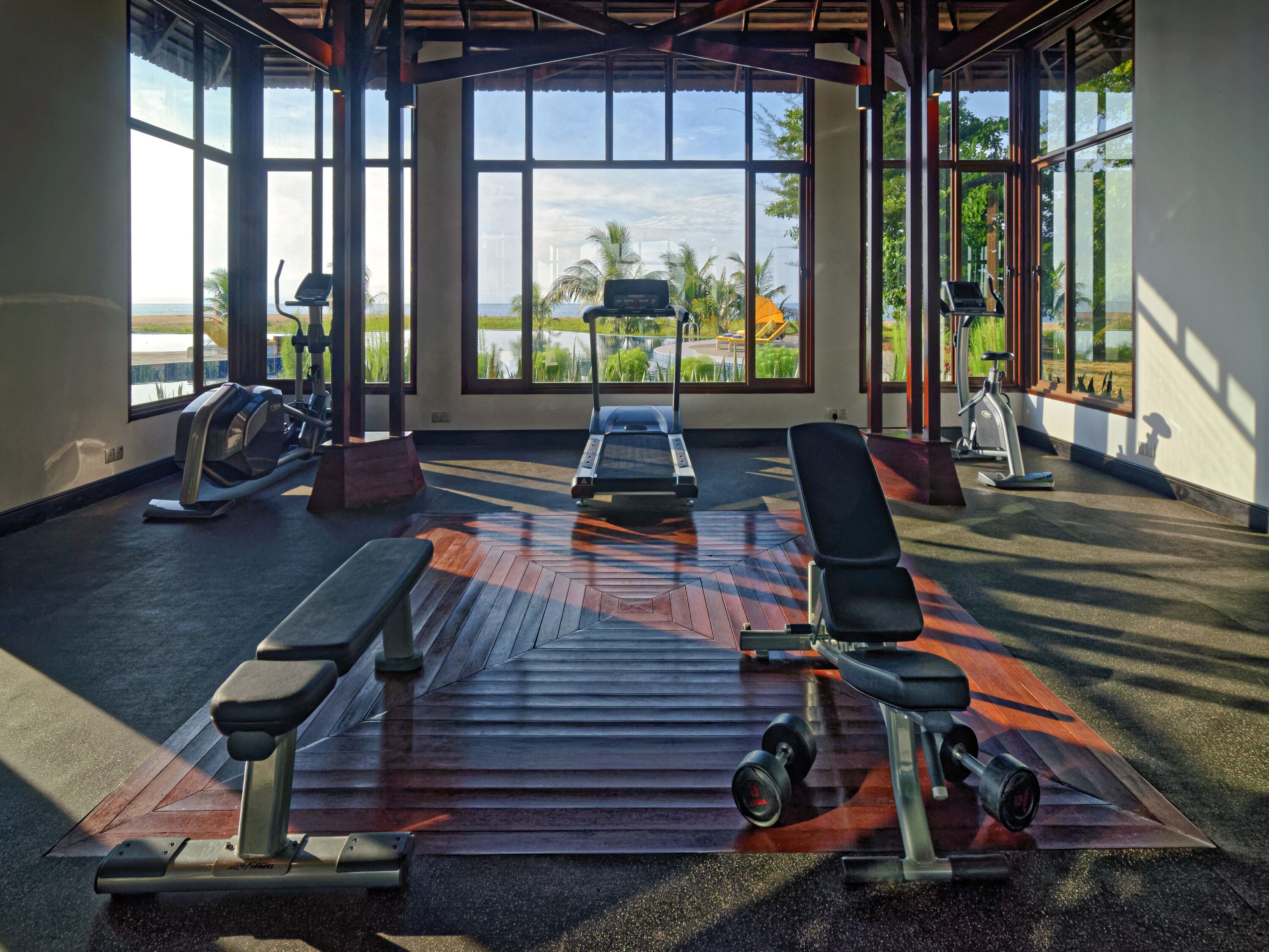 Un gimnasio con equipo de ejercicio, ventanas amplias y vista al mar.