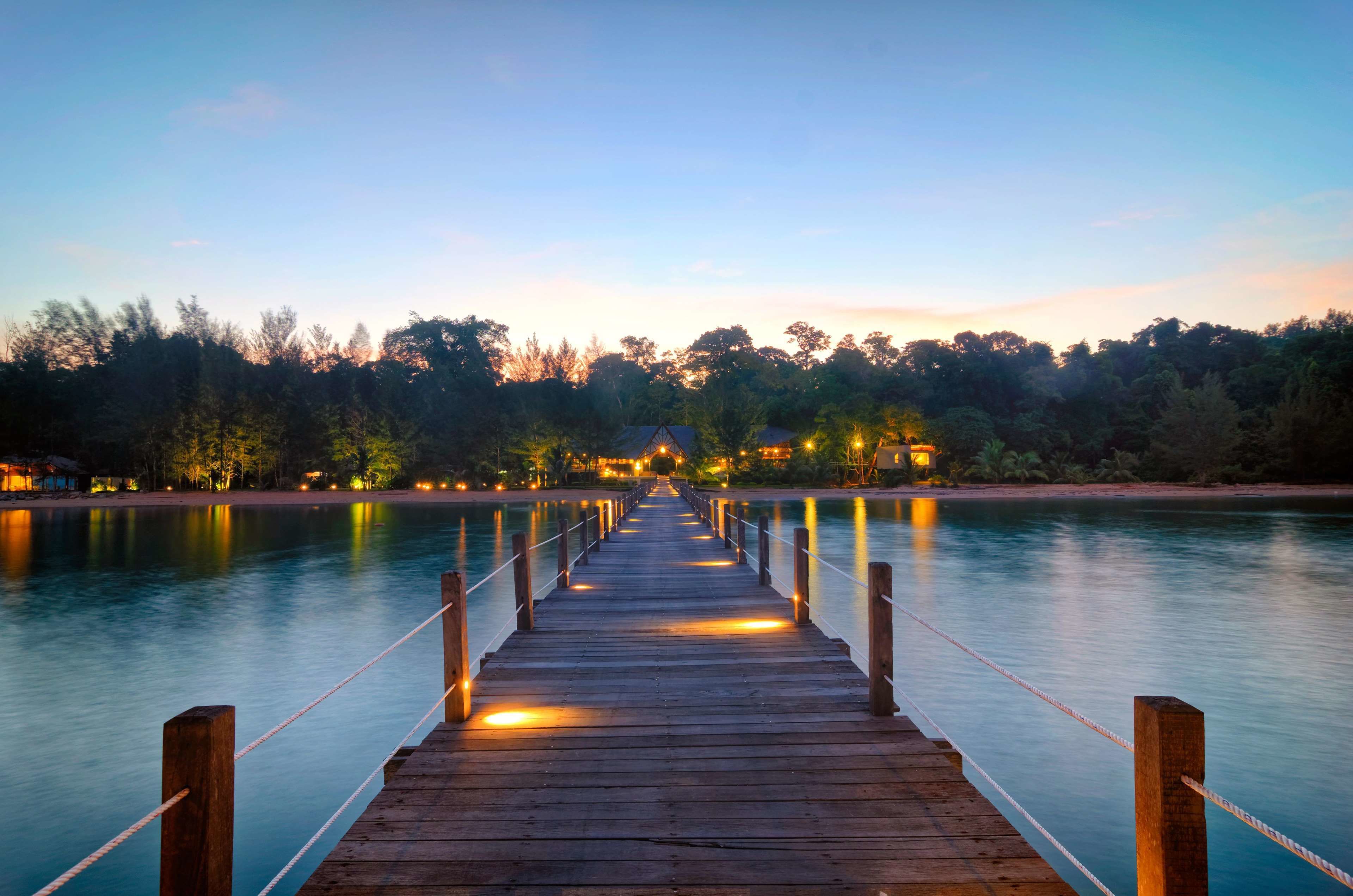 A wooden pier extending into calm water, surrounded by trees and distant buildings.