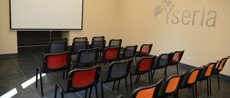 A conference room with rows of chairs, a projector screen, and a logo on the wall.