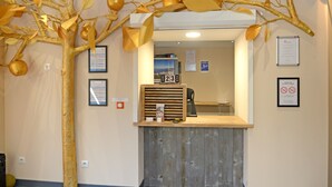 A reception desk with a wooden counter, a large decorative tree with golden leaves and fruits, and several framed notices on the wall. - Logis Hotel Yseria - Historical Center (Agde)