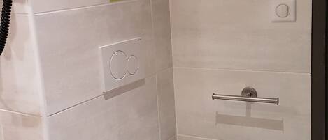 Un baño pequeño y moderno con un inodoro, un secador de manos y un perchero para toallas.