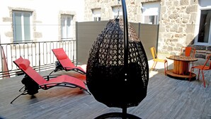 A balcony with red lounge chairs, a black hanging chair, and a wooden table with orange chairs. - Logis Hotel Yseria - Historical Center (Agde)