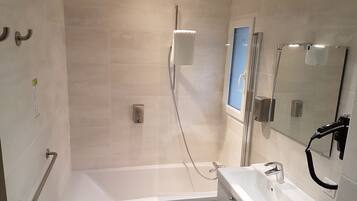 Un baño moderno con cabina de ducha de vidrio, bañera y lavamanos con espejo.