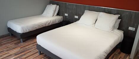 Deux lits simples avec du linge de lit blanc, dans une chambre dotée d’un plancher en bois et d’un mur d’accent rouge.