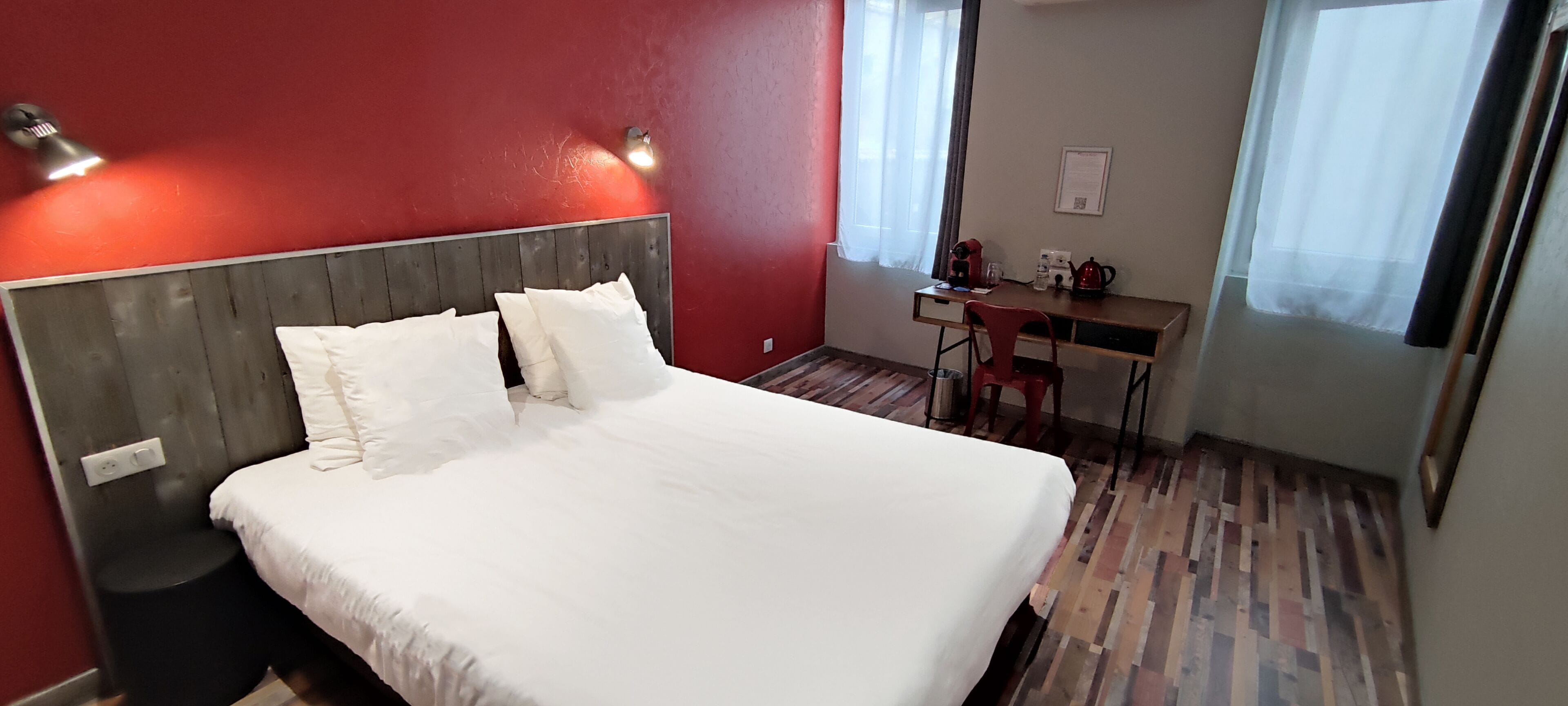 A hotel room with a large bed, a desk with a chair, and a small table with a kettle.