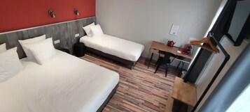 Una habitación de hotel con dos camas individuales, un escritorio de madera, una silla, una mesita pequeña, un hervidor de agua y un televisor.