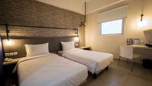 A hotel room with two beds, a desk, a chair, a brick wall, and a window. - Hotel 88 Bekasi By WH (Bekasi)