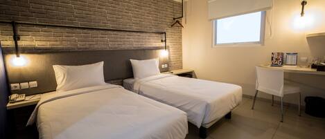 Habitación de hotel con dos camas, un escritorio, una silla, una pared de ladrillo y una ventana.