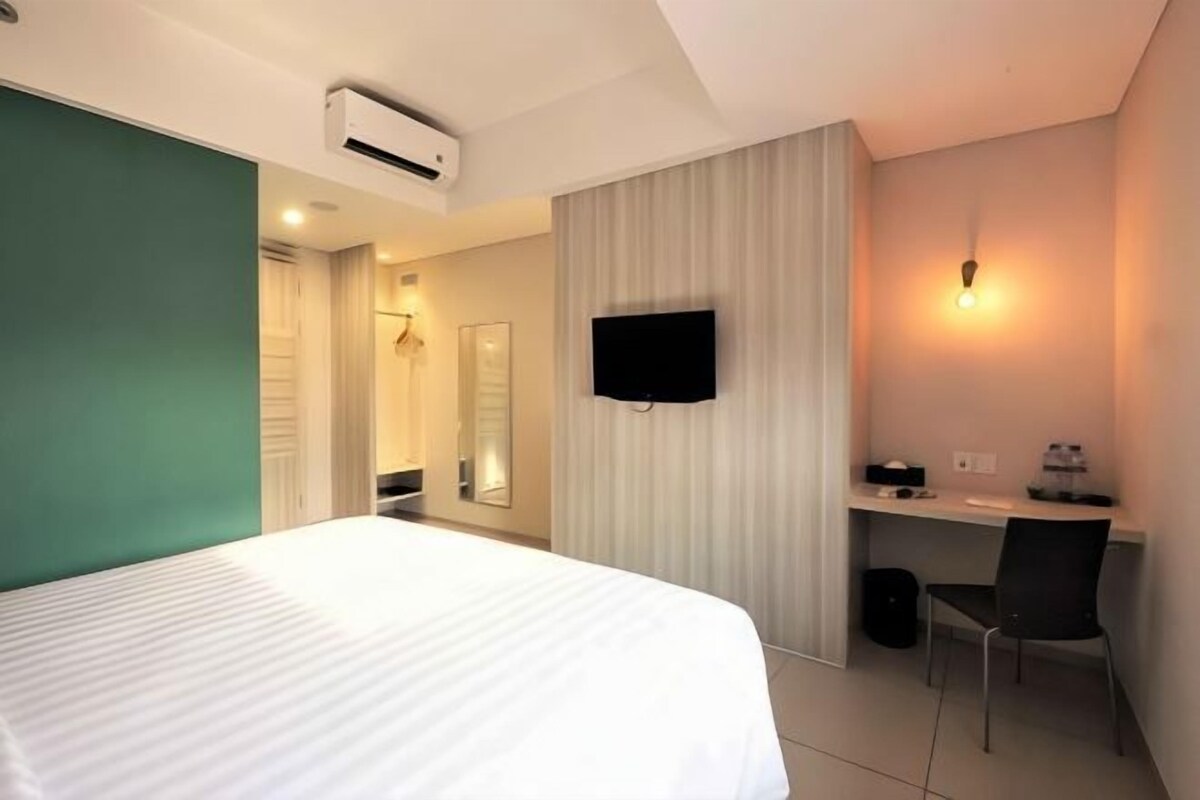 Ein Hotelzimmer mit Bett, Schreibtisch, Stuhl, Fernseher und Spiegel.