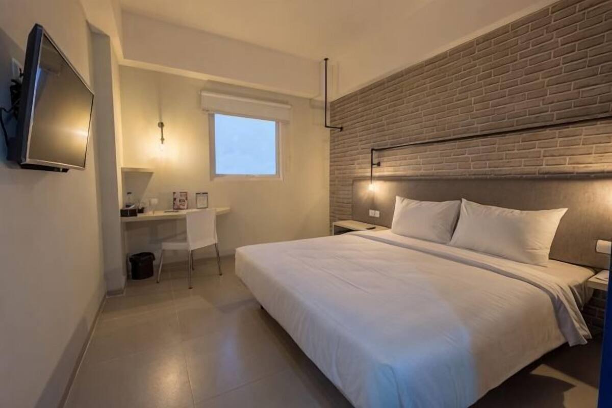 Une chambre à coucher avec un lit, un bureau, une chaise, une télévision et une fenêtre.