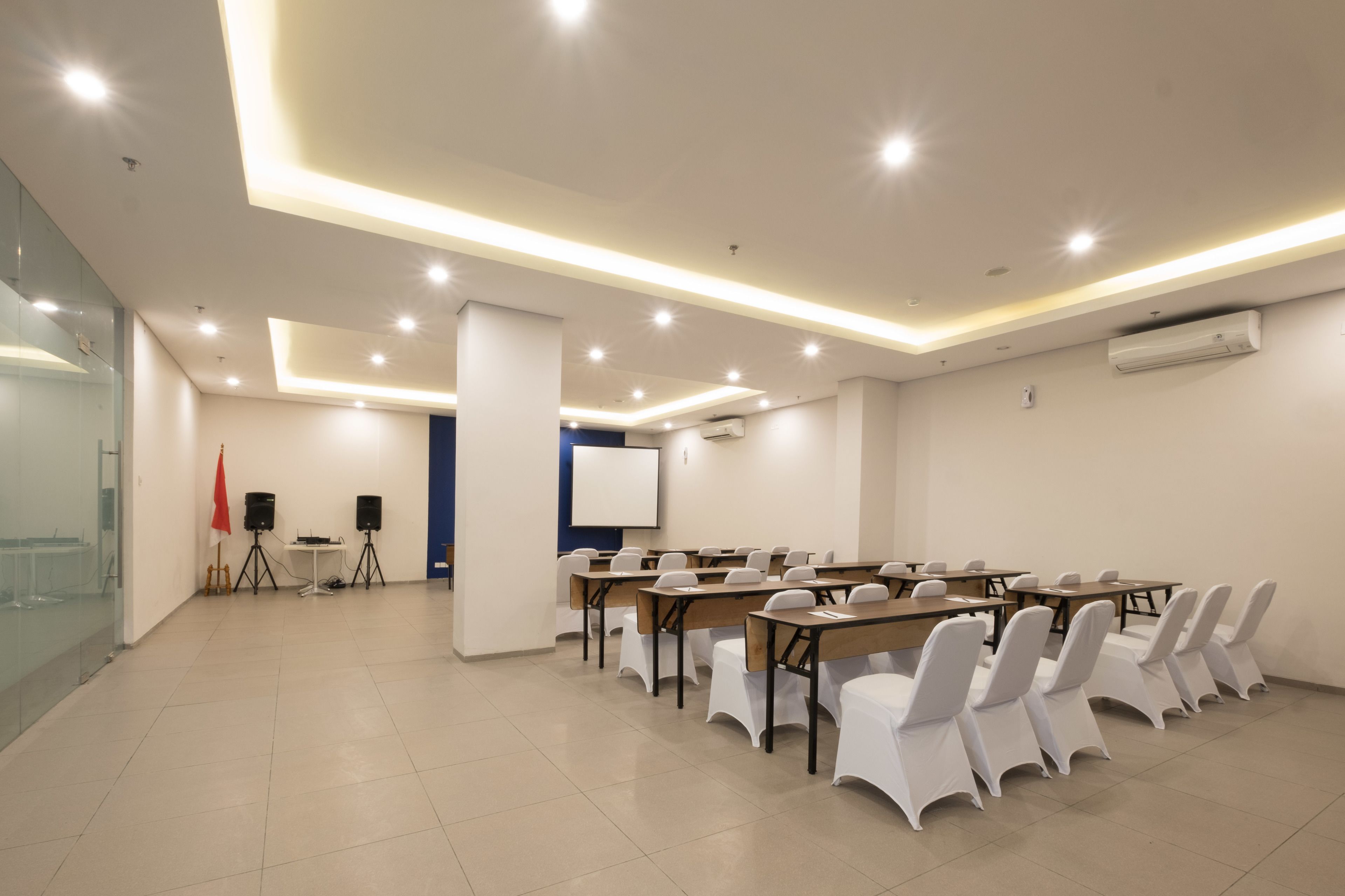 Ein Konferenzraum mit einem langen Tisch, weißen Stühlen und einer Projektionsleinwand.