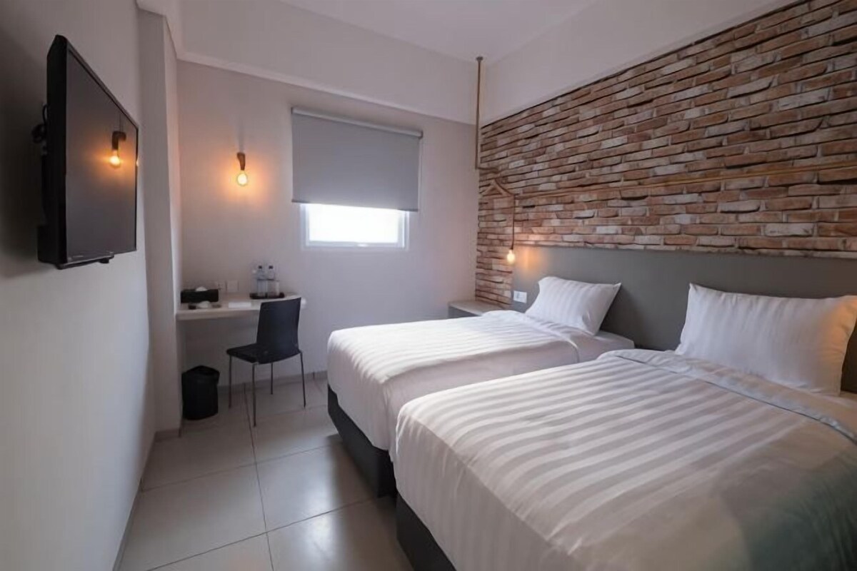 Ein Schlafzimmer mit zwei Betten, einem Schreibtisch, einem Stuhl, einem Fernseher und einer Ziegelwand.