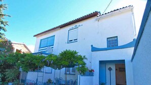 Un patio con un edificio blanco, contraventanas azules y plantas en macetas.