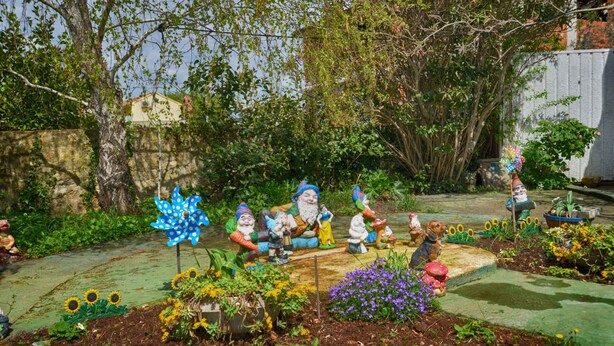 Un jardín con estatuillas de gnomos, un molinillo de viento y diversas plantas.