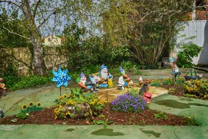 Un jardin agrémenté de statues de gnomes, d’une girouette et de différentes plantes.