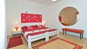 Un dormitorio con una cama blanca, ropa de cama roja, un espejo redondo y un banco rojo.