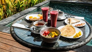 Un desayuno junto a la piscina, con una mesa, platos, tazones y bebidas.
