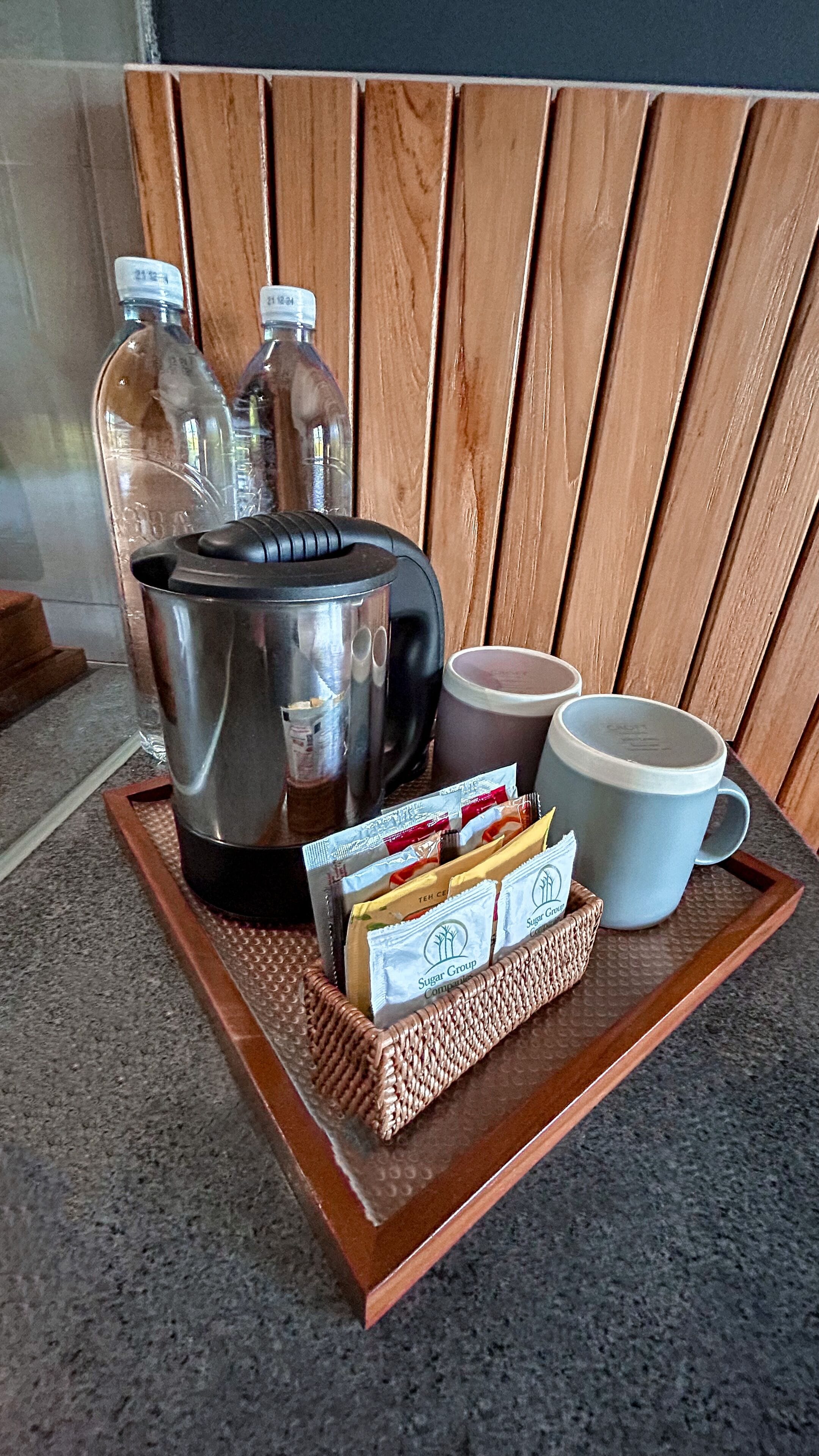 Una bandeja con una cafetera, dos botellas, una taza y sobres de azúcar sobre un tapete texturizado.