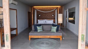 Un dormitorio con cabecera de madera, cama con ropa de cama gris, dos lámparas de noche, una ventana con vistas y una alfombra circular en el suelo.